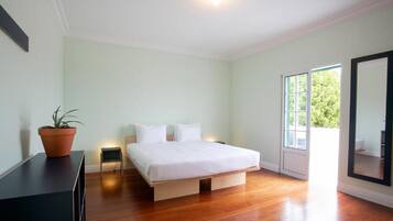 A bedroom with a bed, a potted plant, a small bedside table, and a large window.