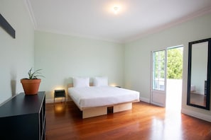 A bedroom with a bed, a potted plant, a small bedside table, and a large window. - Salt Lips (Ponta Delgada)