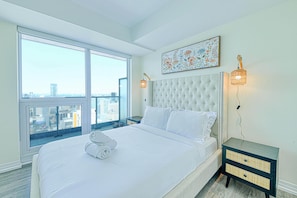 A hotel room with a large bed, a view of the city, and a decorative wall piece.