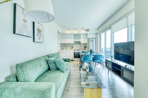 Ein modernes Wohnzimmer mit einem grünen Sofa, einem Glastisch und einem Essbereich mit blauen Stühlen.