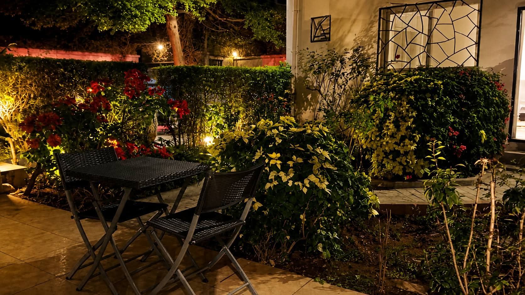 Un espace extérieur aménagé avec une table et des chaises, entouré d’une végétation luxuriante et de plantes en fleurs.