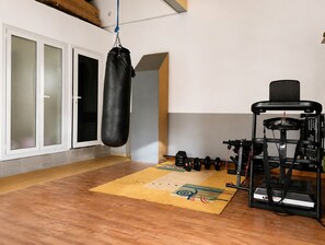 Een sportschool met een bokszak, een gewichtbank en diverse fitnessapparaten.