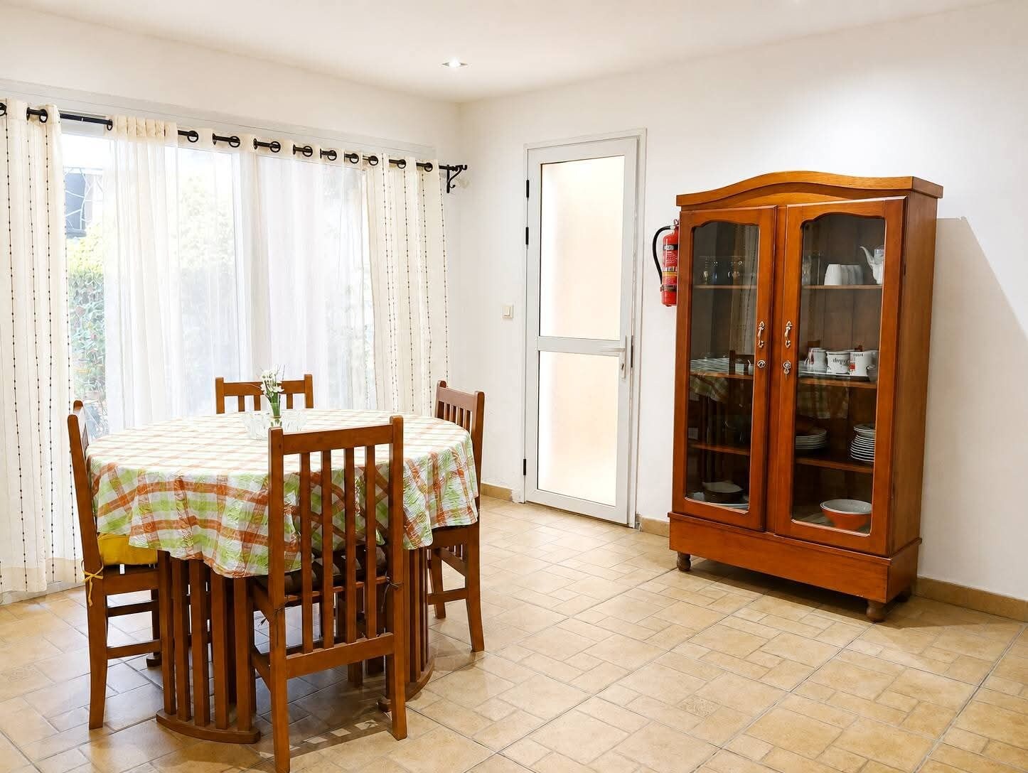 A dining area with a table set for four, a wooden cabinet with glass doors, and a door leading outside.
