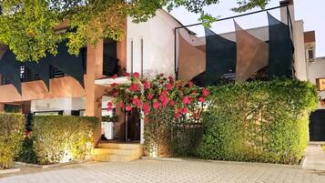 A building with a modern architectural design, featuring a staircase leading to an entrance, surrounded by well-maintained hedges and flowering plants.
