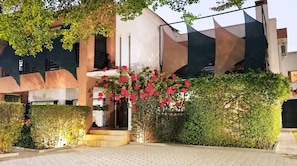 A building with a modern architectural design, featuring a staircase leading to an entrance, surrounded by well-maintained hedges and flowering plants.