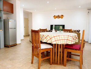 Ein Essbereich mit kariertem Tischleinentuch, Holzkästen, einem Fernseher und einem Kühlschrank.