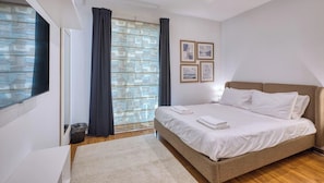A bedroom with a bed, a window with curtains, a wall with framed pictures, and a wooden floor. - Siggiewi 3BR Penthouse with Two Terraces & WIFI (Siġġiewi)