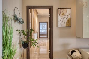 A hallway with a wooden door leading to a bedroom, a potted plant, a wall-mounted abstract painting, and a white cabinet. - Siggiewi 3BR Penthouse with Two Terraces & WIFI (Siġġiewi)