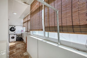 A laundry room with a washing machine, dryer, and a window with bamboo blinds. - Siggiewi 3BR Penthouse with Two Terraces & WIFI (Siġġiewi)