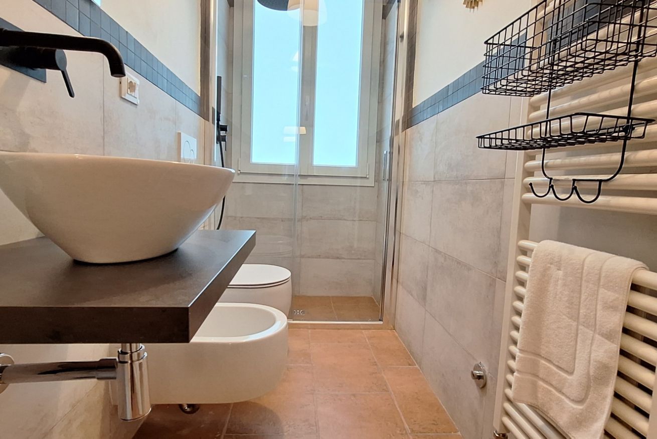 Ein Badezimmer mit einem großen Waschbecken, Toilette und Dusche. Ein Handtuchhalter und ein Fenster sind vorhanden.