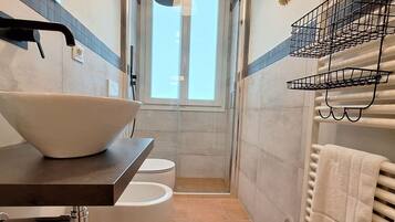 Ein Badezimmer mit einem großen Waschbecken, Toilette und Dusche. Ein Handtuchhalter und ein Fenster sind vorhanden.