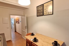 Et spiseområde med et træbord og stole, en dør der fører til et andet rum, samt to indrammede botaniske tryk på væggen.