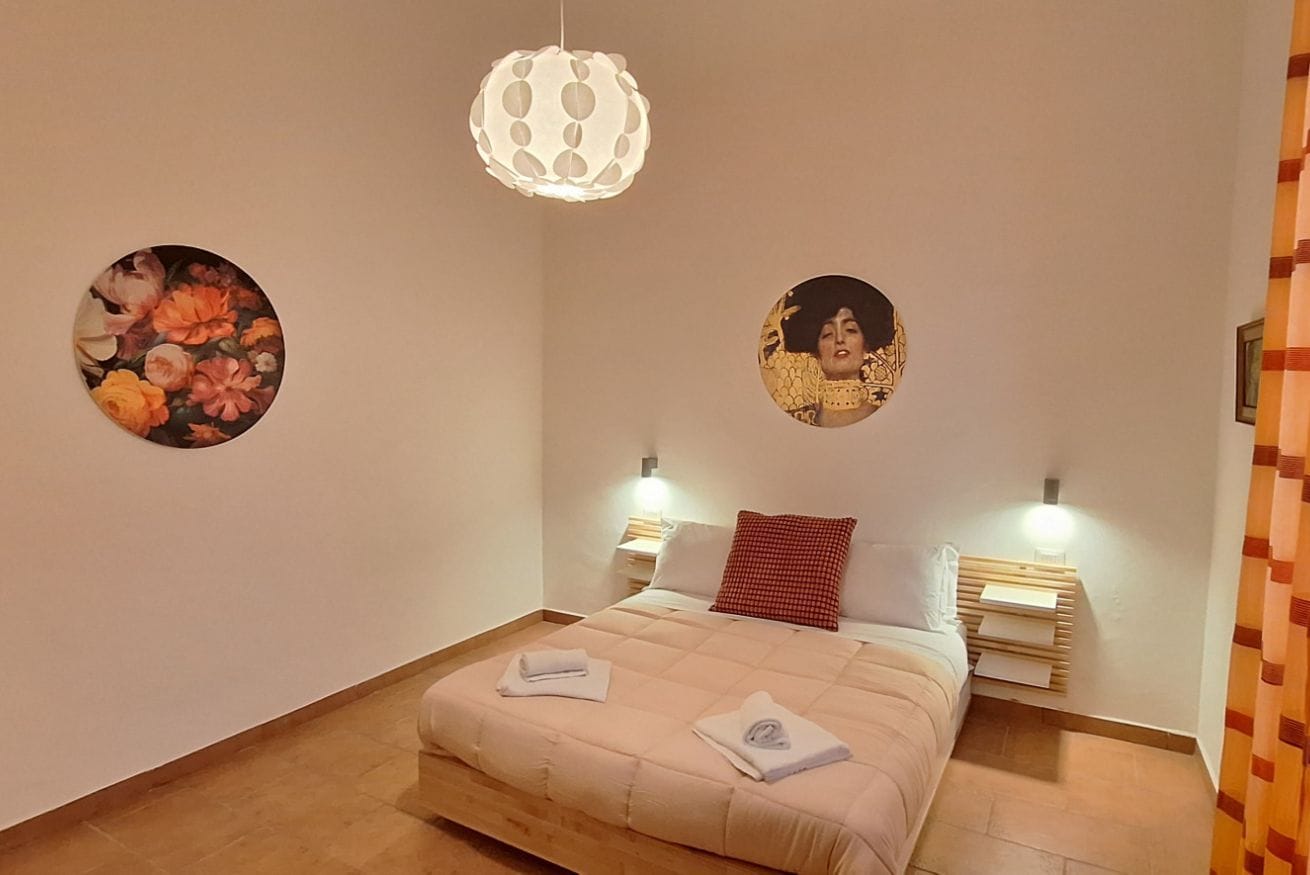 A bedroom with a bed, two bedside tables, a wall-mounted lamp, and two circular wall art pieces.