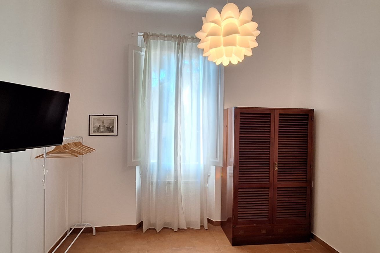 Una habitación con una televisión sobre un mueble bajo, un armario de madera, una cortina y una lámpara colgante.