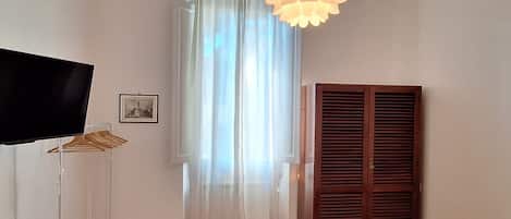 Una habitación con una televisión sobre un mueble bajo, un armario de madera, una cortina y una lámpara colgante.