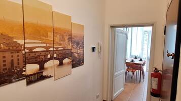 Un couloir orné d’un tableau représentant un paysage urbain, un coin repas avec des chaises et une table, et un extincteur fixé au mur.