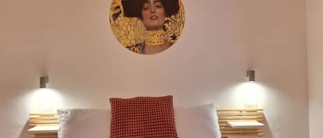 A bedroom with a bed, two bedside tables, a wall-mounted light, and a circular artwork above the bed.