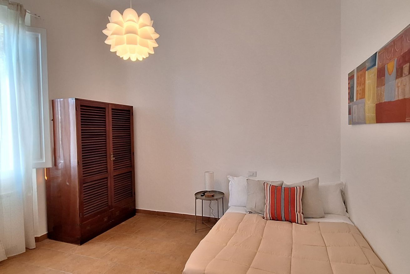 A bedroom with a bed, a wardrobe, a small table, and a hanging light fixture.