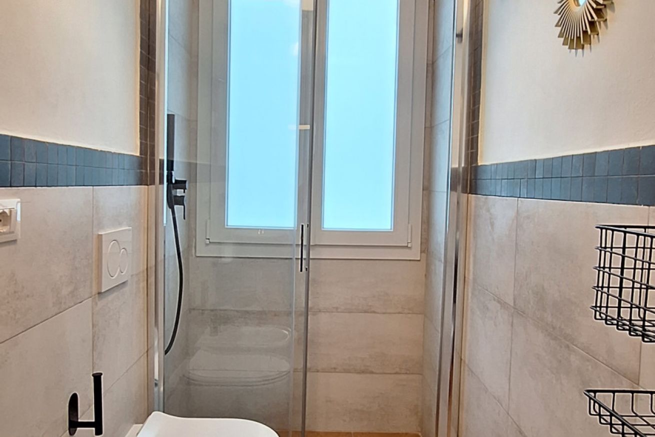 Un bagno con cabina doccia in vetro, un water e un portascopino.