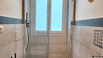 Un bagno con cabina doccia in vetro, un water e un portascopino.