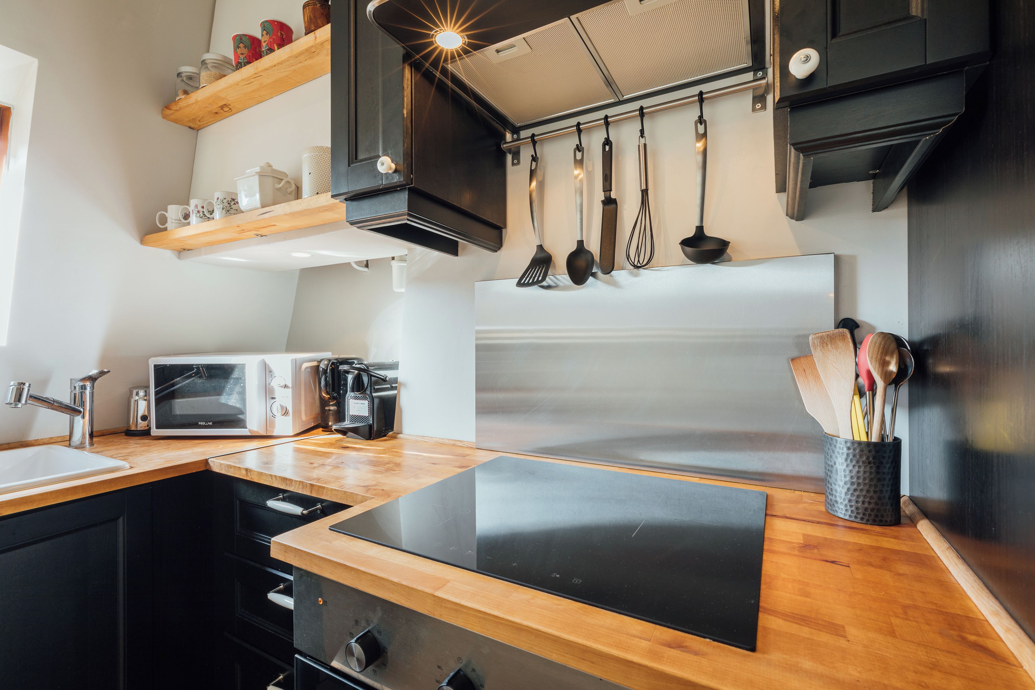 Een moderne keuken met een houten aanrecht, een ingebouwde magnetron, een roestvrijstalen koelkast en hangend keukengerei.