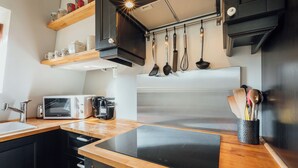 Cozinha moderna com bancada de madeira, micro-ondas embutido, frigorífico em aço inoxidável e utensílios pendurados.