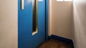 Um corredor com porta azul, janela com persianas e piso de madeira.