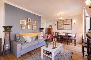 Een woonkamer met een grijze bank, een houten salontafel en een eetgedeelte met houten stoelen en een tafel.