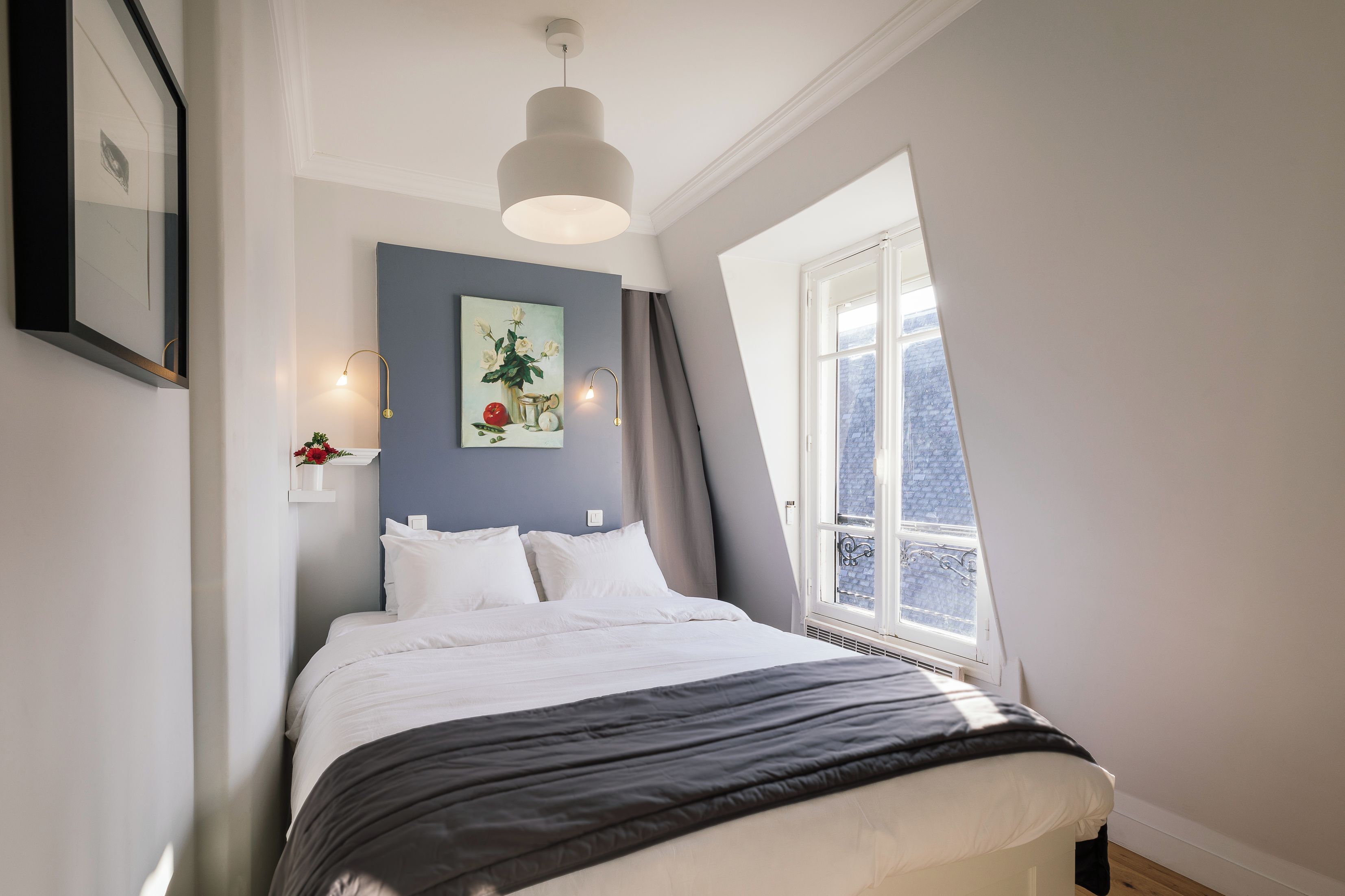 Een slaapkamer met een bed, een raam, een schilderij en een lamp.