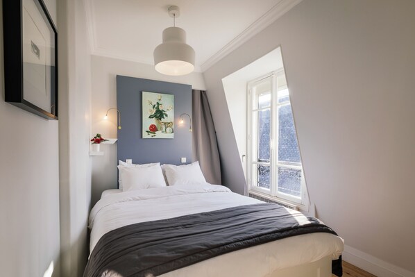 Een slaapkamer met een bed, een raam, een schilderij en een lamp.