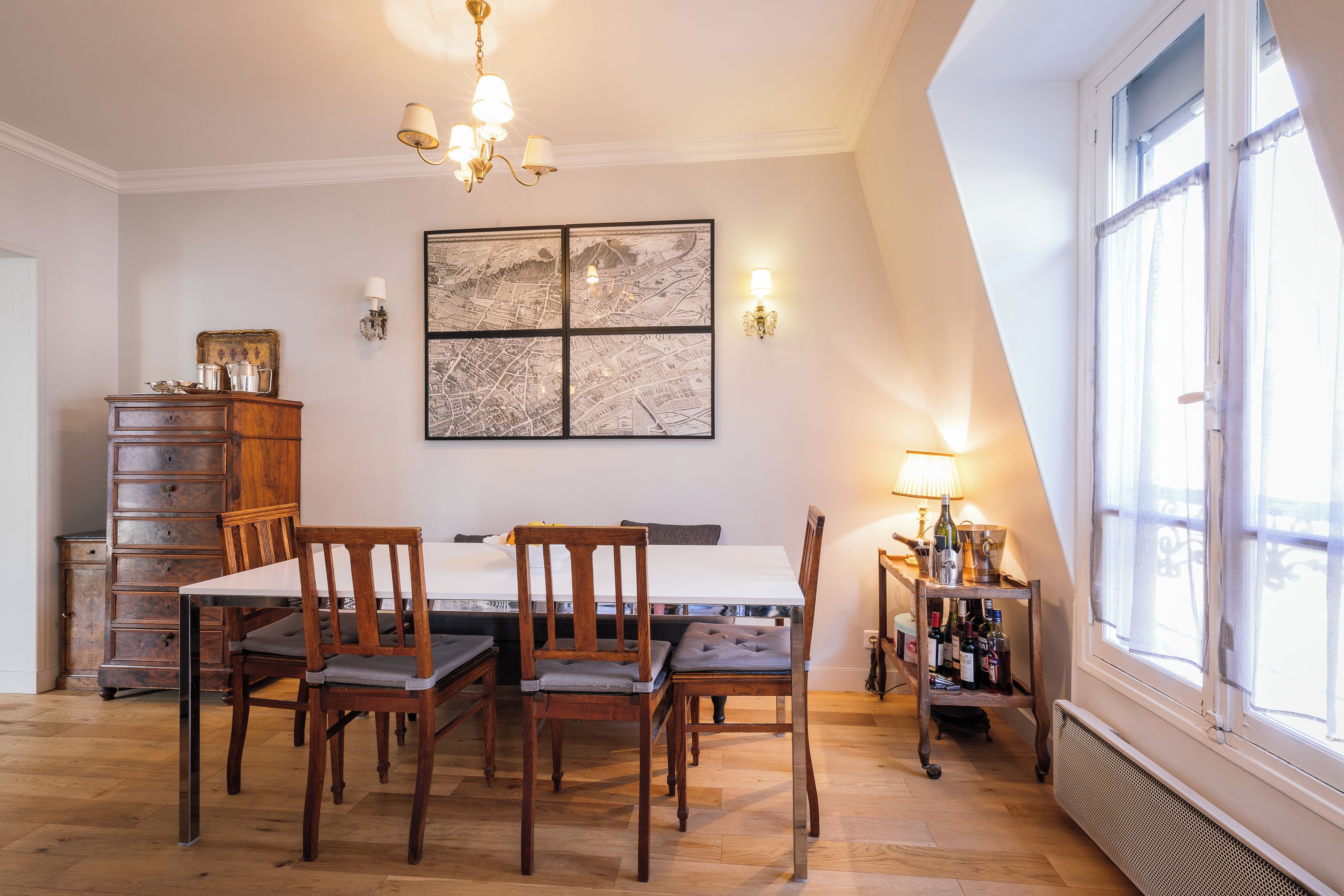 A dining area with a wooden table, chairs, a chandelier, a map artwork, and a wine rack.