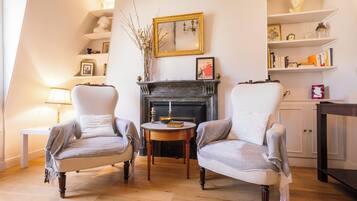 Un salon traditionnel avec deux fauteuils, une cheminée, une table avec une bougie et une bibliothèque.