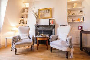 A traditional living room with two armchairs, a fireplace, a table with a candle, and a bookshelf.