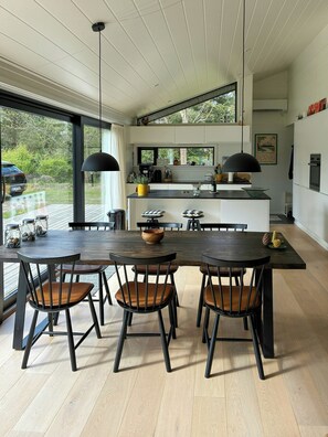 A modern kitchen with a central island, wooden dining table with chairs, and a view of the outdoors. - Family summer house with direct beach access (Nykøbing SJ)