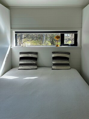 Ein Schlafzimmer mit einem Bett, zwei Kissen, einem Fenster und einer Lampe.