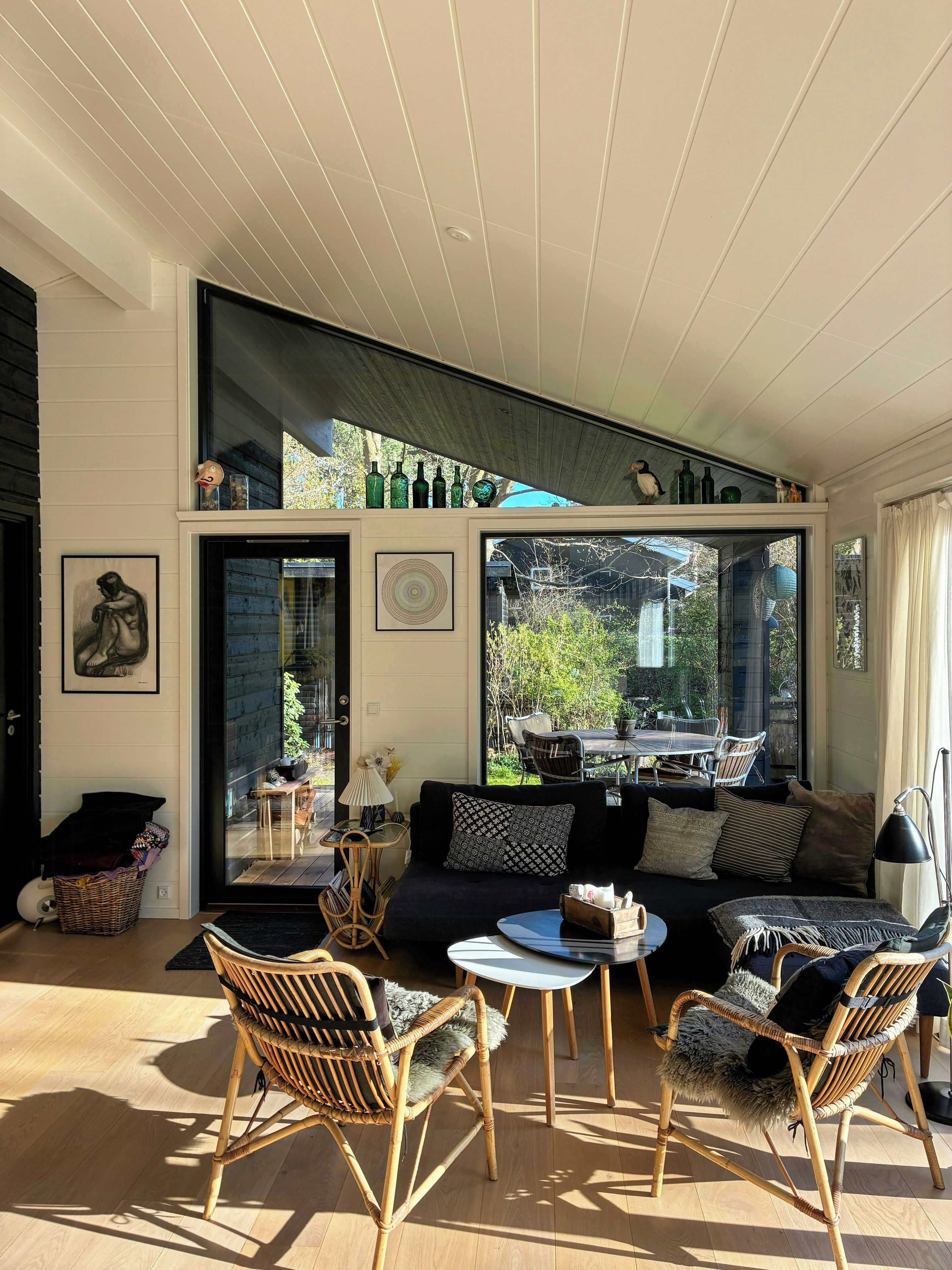 Una habitación soleada con un sofá, dos sillones de mimbre, una mesita y un amplio ventanal con vistas al exterior.