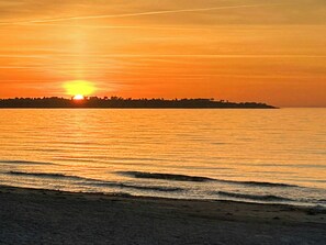 A sunset over a calm sea with a distant shoreline silhouette. - Family summer house with direct beach access (Nykøbing SJ)