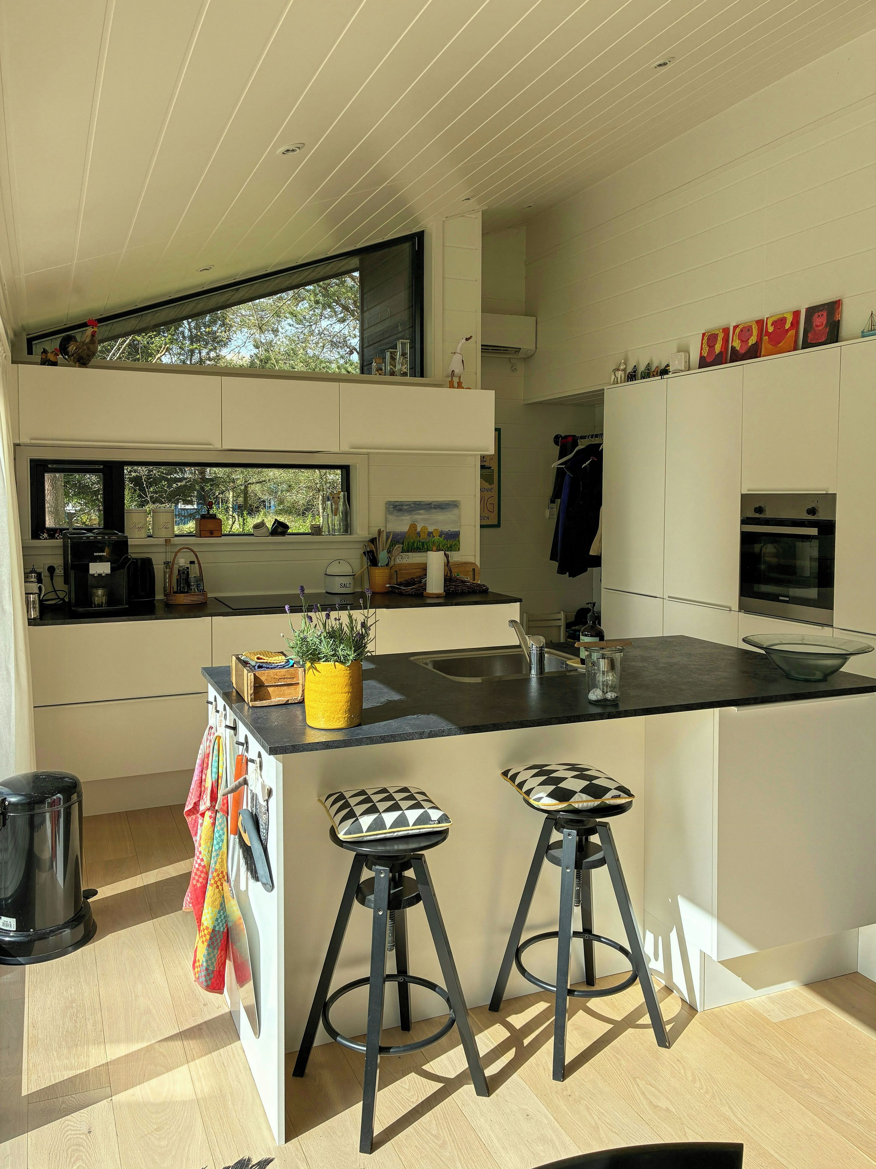 A modern kitchen with a central island, bar stools, and a view of the outdoors.