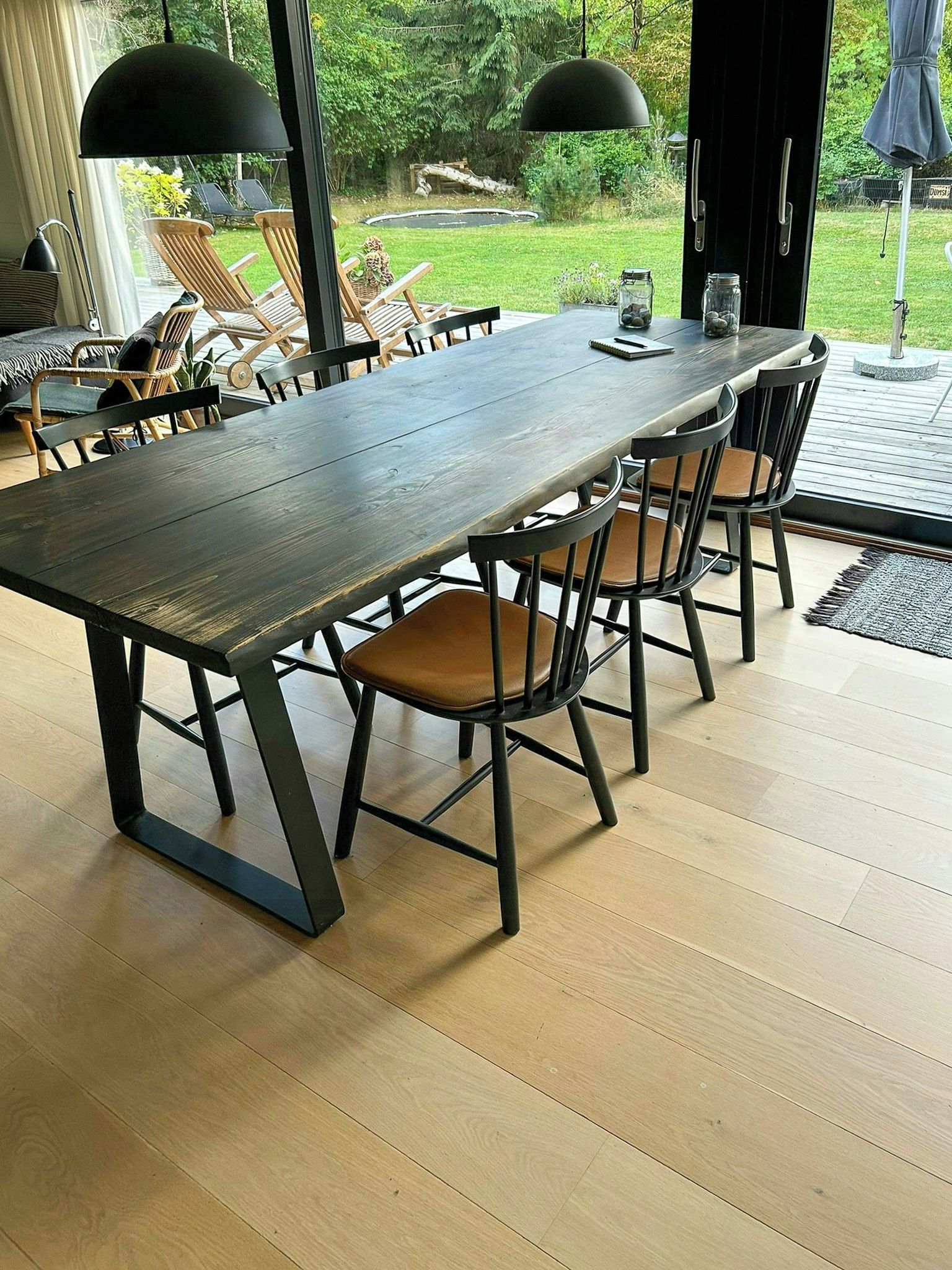 Una larga mesa de comedor con sillas, una lámpara negra y vistas al exterior.