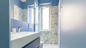 A bathroom with a white sink, a mirror, and a shower area. - Luciano Boutique Apartment (Roma)