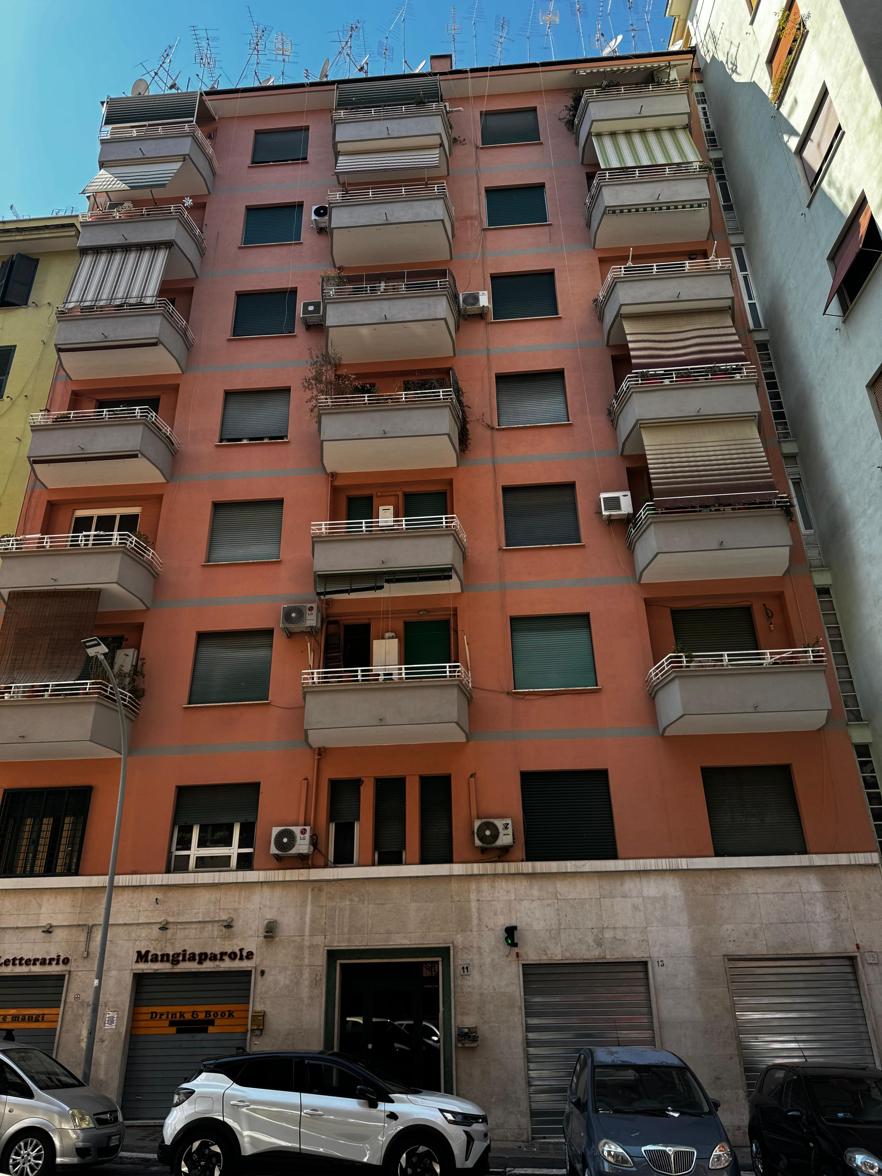Un edificio residencial de varios pisos con balcones, unidades de aire acondicionado y una tienda en la planta baja con un letrero.