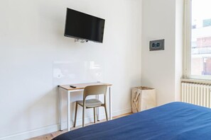 Un dormitorio con cama, escritorio, silla, televisor y ventana.