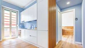 A modern kitchen with white cabinets, a wooden floor, and a sliding door leading to a balcony. - Luciano Boutique Apartment (Roma)
