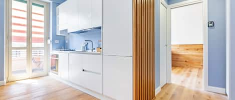 Una cocina moderna con armarios blancos, piso de madera y puerta corrediza a un balcón.
