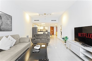 Ein modernes Wohnzimmer mit einer Couch, einem Couchtisch, einem Fernseher und einer Küche im Hintergrund.