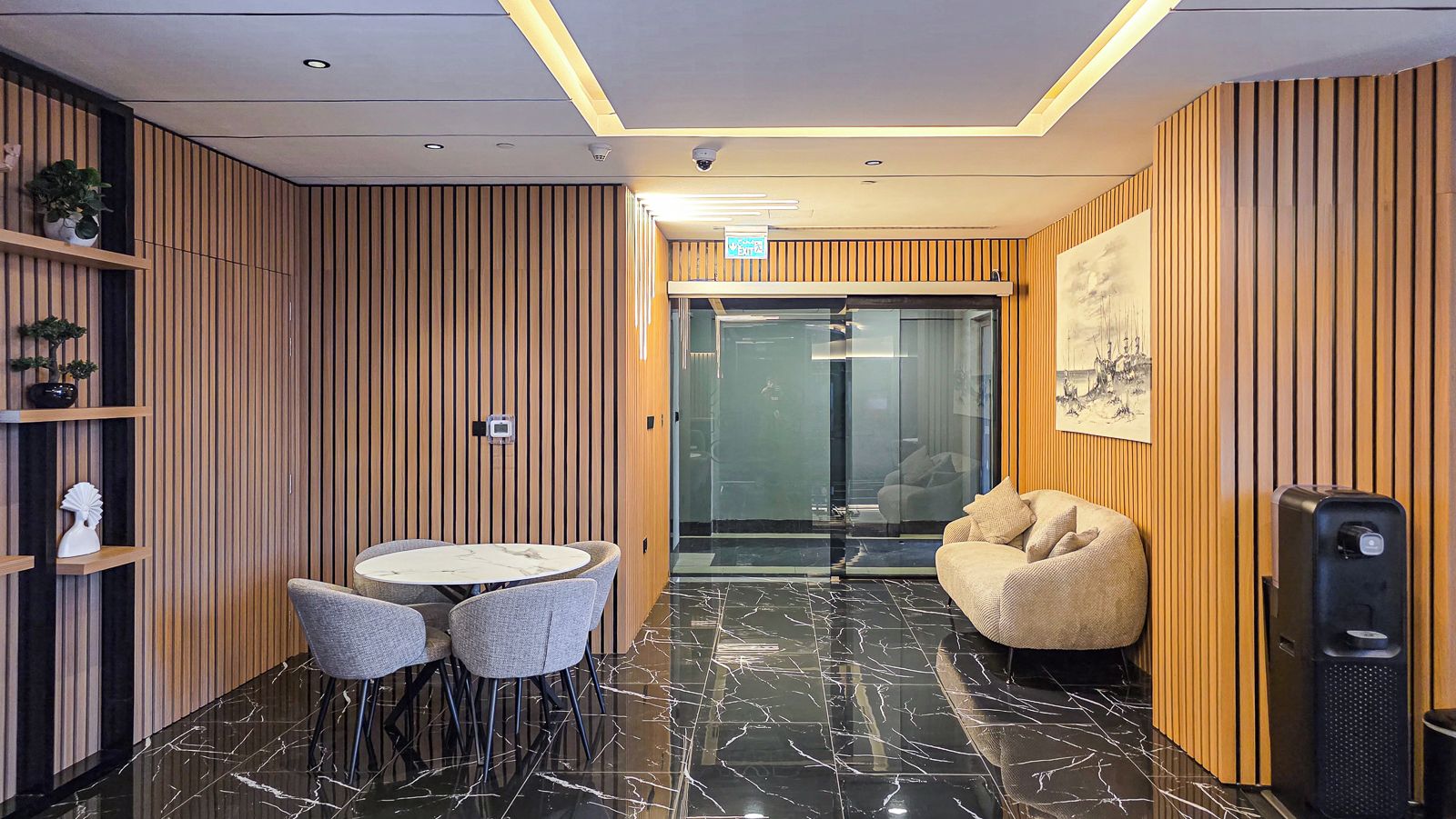 Un interior moderno con una mesa redonda y sillas, un sillón informal, paneles de madera y un dispensador de agua.