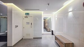 Un passadís amb una porta indicada amb un senyal d'emergència, una banca i un corredor que condueix a una altra zona.