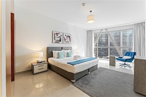 Ein modernes Hotelzimmer mit einem großen Bett, Nachttischen, einem Schreibtisch, einem Sessel und Blick auf die Stadt durch große Fenster.