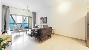 Ein modernes Wohnzimmer mit einer Couch, einem Sessel und einem Couchtisch. Es gibt ein großes Fenster mit Vorhängen, eine Deckenleuchte und ein Bild an der Wand.