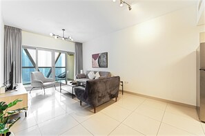 Un soggiorno moderno con divano, poltrona e tavolino. Si nota un'ampia finestra con tende, un lampadario a soffitto e un quadro appeso al muro.